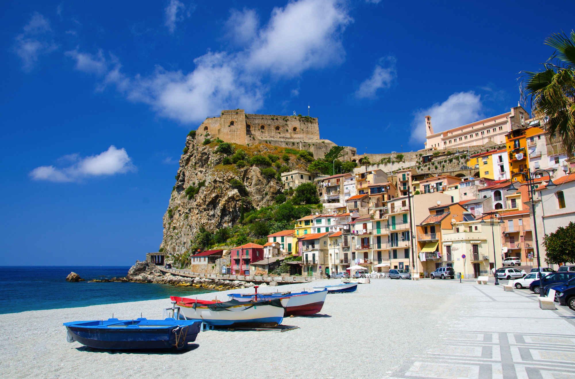 Fishing colorful boats on sandy beach of Tyrrhenian sea coast shore of beautiful seaside town Scilla with traditional houses and old medieval castle on rock Castello Ruffo, Calabria, Southern Italy
