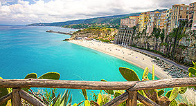 Tropea town and Tyrrhenian Sea beach, colorful buildings on top of high big rocks, view from Sanctuary church of Santa Maria dell Isola with fence foreground, Vibo Valentia, Calabria, Southern Italy