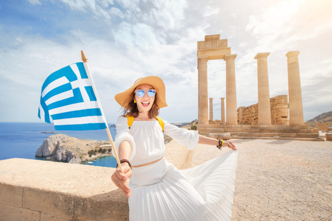 Woman Traveler with backpack Enjoying great view og the ancient Greek Acropolis with flag in hands