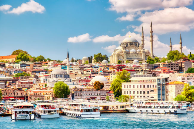 Touristic sightseeing ships in Golden Horn bay of Istanbul and view on Suleymaniye mosque with Sultanahmet district against blue sky and clouds. Istanbul, Turkey during sunny summer day