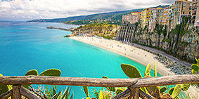Tropea town and Tyrrhenian Sea beach, colorful buildings on top of high big rocks, view from Sanctuary church of Santa Maria dell Isola with fence foreground, Vibo Valentia, Calabria, Southern Italy